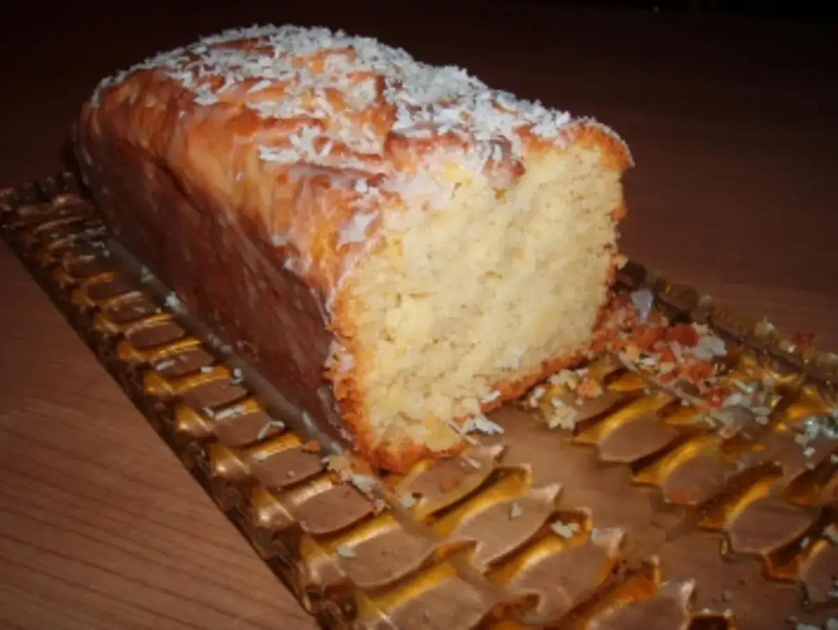 Ein saftiger ananas kokos kuchen mit Zuckerguss und Kokosraspeln, auf einem goldenen Servierteller.