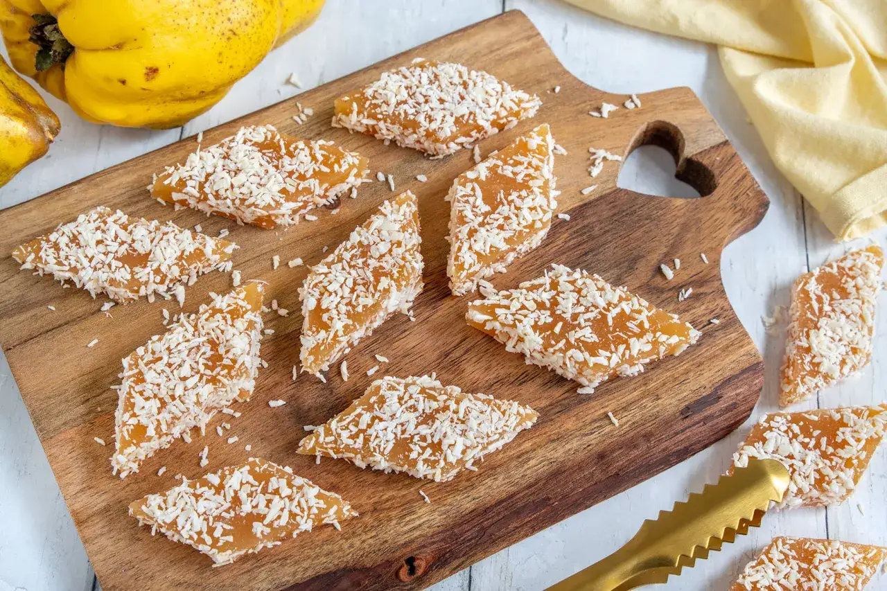 Quittenbrot-Stücke mit Kokosraspeln bestreut auf einem Holzbrett. Ein einfaches Rezept für Quittenbrot.