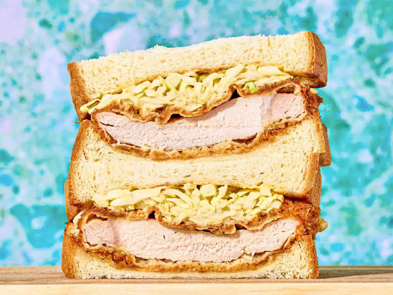 Ein gestapeltes Katsu Sando mit knusprigem paniertem Schweinefleisch, Kohl und cremiger Sauce zwischen weichem Toastbrot.