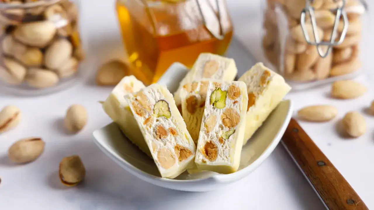 Weißer Nougat mit Pistazien und Mandeln, der zeigt, aus was Nougat besteht: Nüsse, Honig und Zucker.