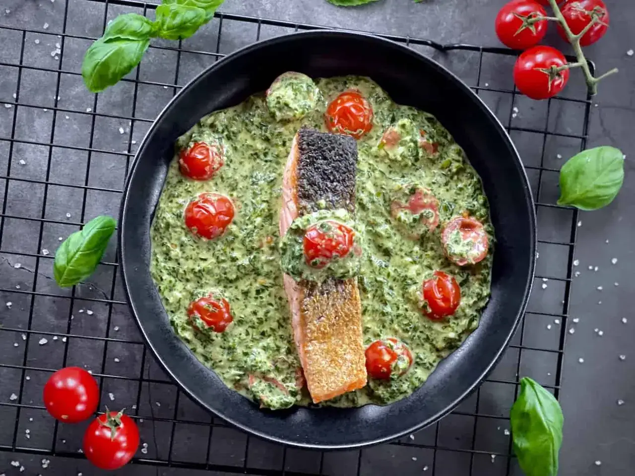 Lachs mit Spinat und Tomaten in cremiger Sauce, garniert mit frischem Basilikum und Kirschtomaten.
