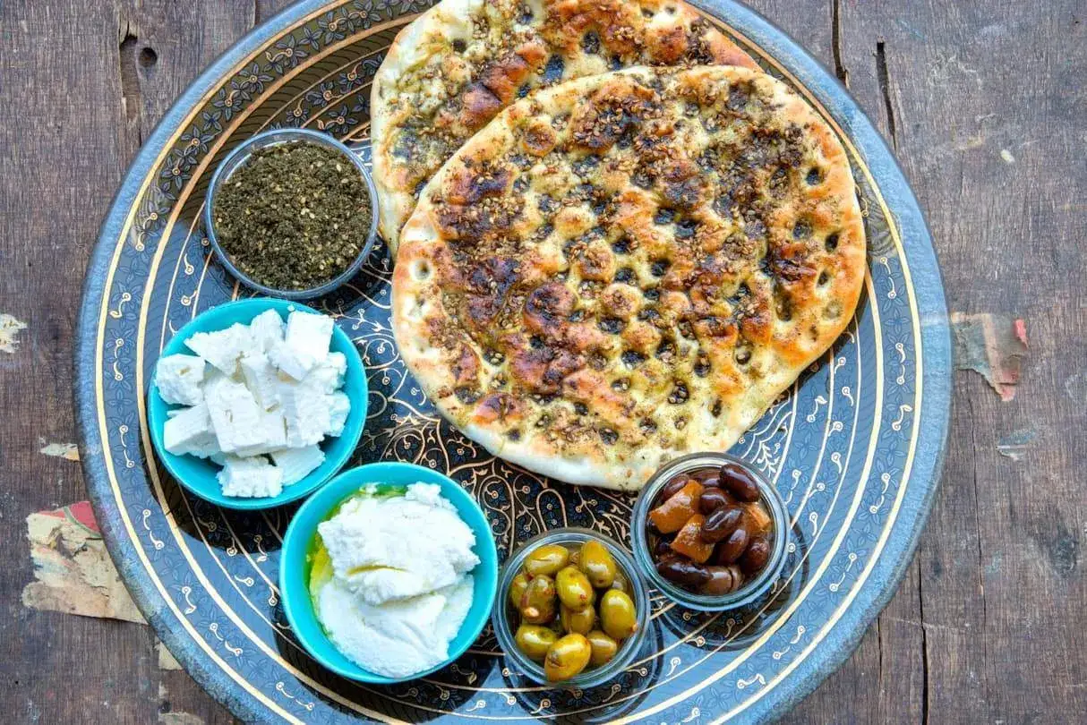 Fladenbrot mit Zatar, Oliven, Feta und Frischk&auml;se auf einem dekorativen Teller. Zatar ist eine w&uuml;rzige Mischung aus Kr&auml;utern, Sesam und Sumach.