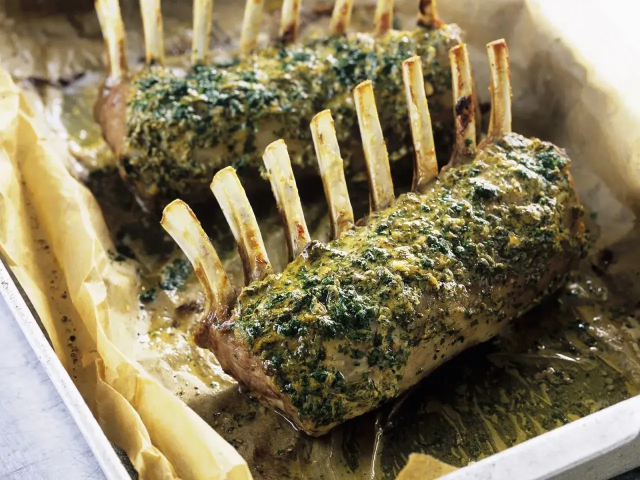 Zwei Lammkarrees, mit Kr&auml;utern und Senf bestrichen, auf Backpapier in einer Metallschale. Das lammkarree bestes rezept f&uuml;r einen Festtagsschmaus.