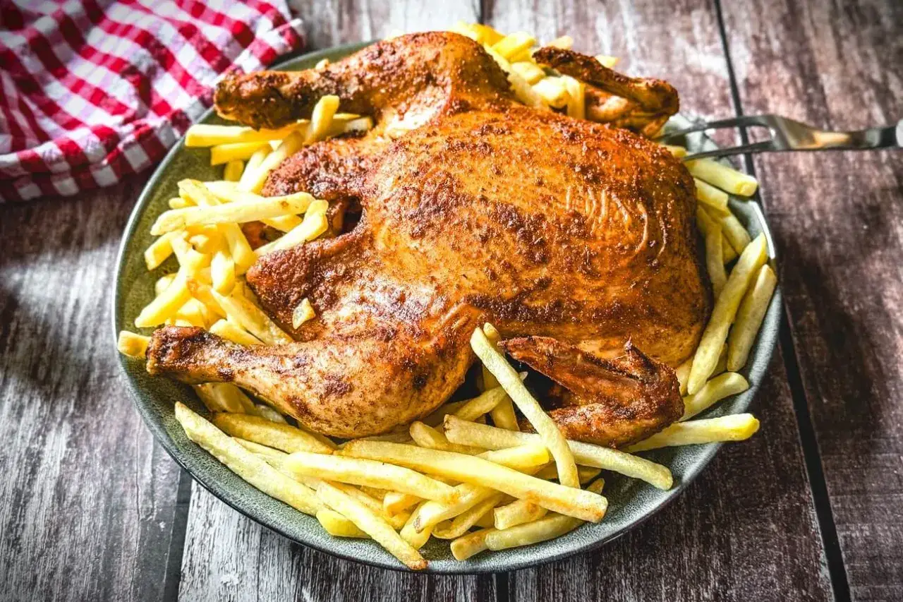 Ein knuspriger poulet roti, goldbraun gebraten, liegt auf einem Bett aus knusprigen Pommes Frites auf einem Teller.