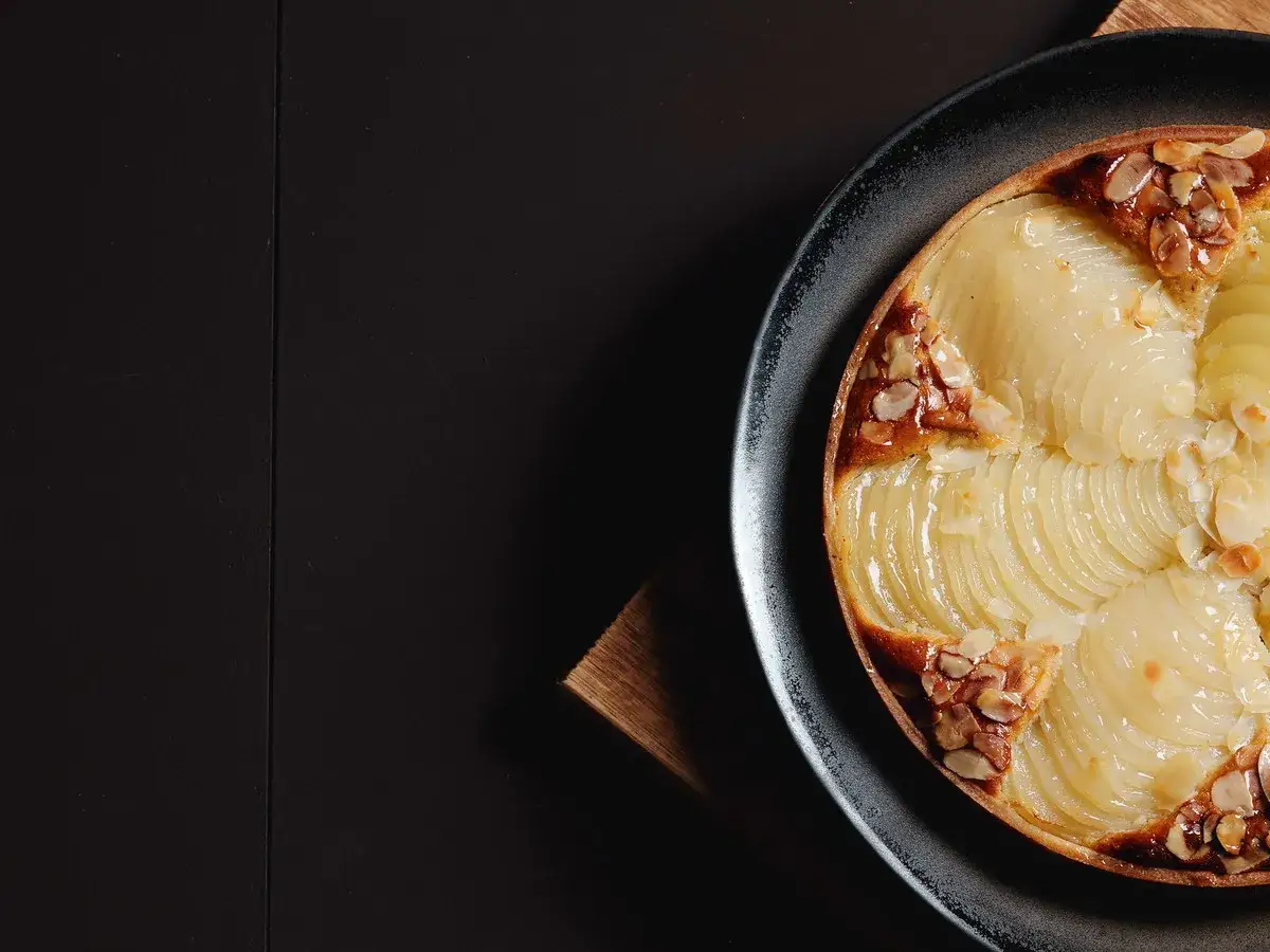 Eine k&ouml;stliche Tarte Bourdaloue mit zarten Birnenspalten und ger&ouml;steten Mandelsplittern auf einem dunklen Teller.
