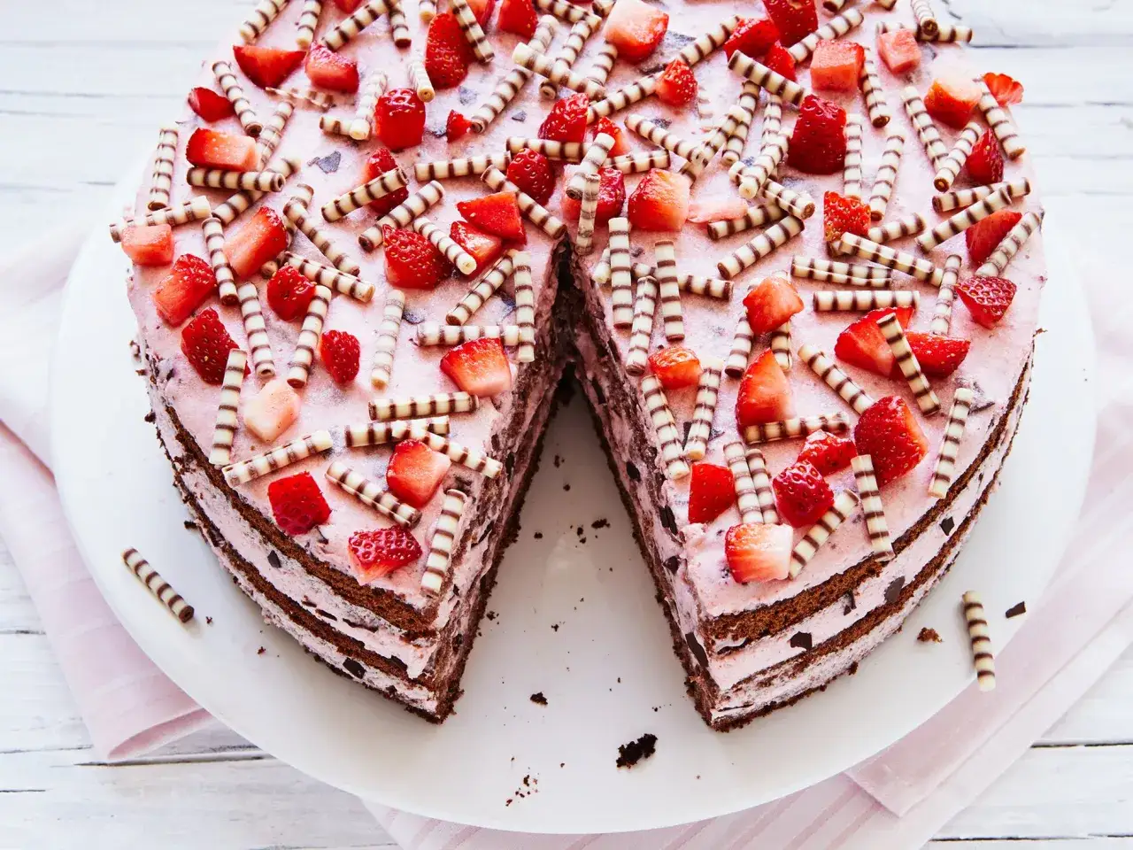 Eine köstliche Erdbeer Stracciatella Torte, dekoriert mit frischen Erdbeeren und Schokoröllchen, wartet darauf, angeschnitten zu werden.