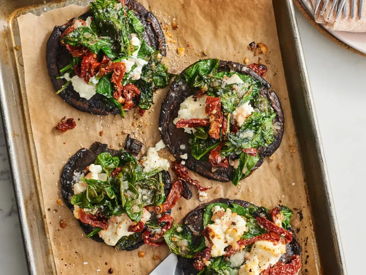 Vier gefüllte Portobello Pilze mit Spinat, getrockneten Tomaten und Käse auf einem Backblech.