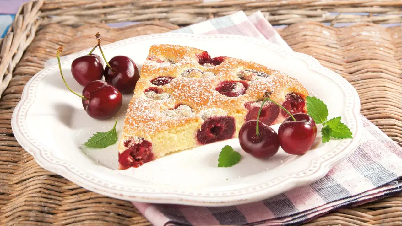 Ein St&uuml;ck saftiger Clafoutis aux cerises, best&auml;ubt mit Puderzucker, garniert mit frischen Kirschen und Minze.