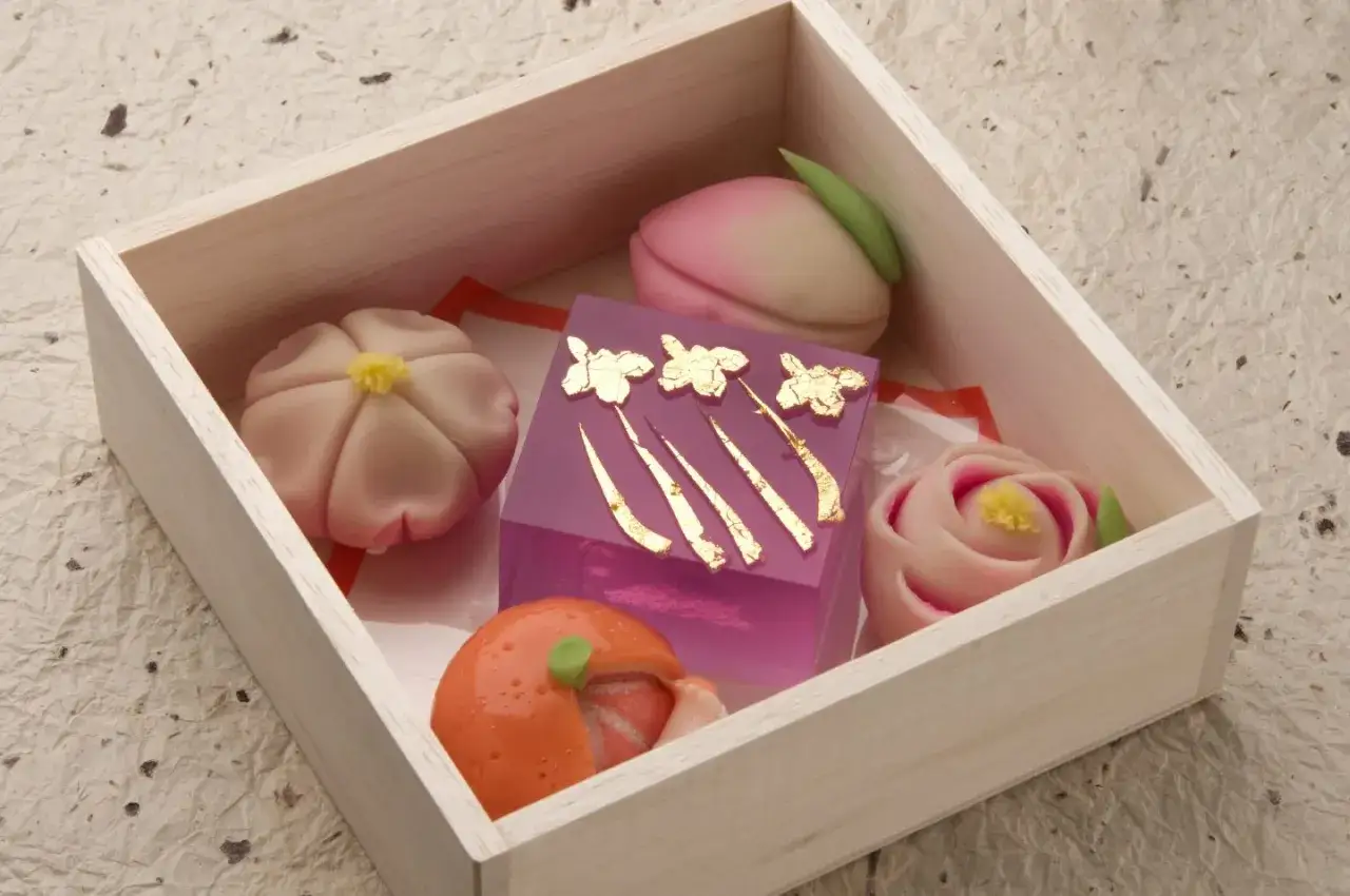 Schachtel mit kunstvollen japanischen Desserts: Bl&uuml;ten, Pfirsich, Rose und eine Frucht, verziert mit Blattgold.