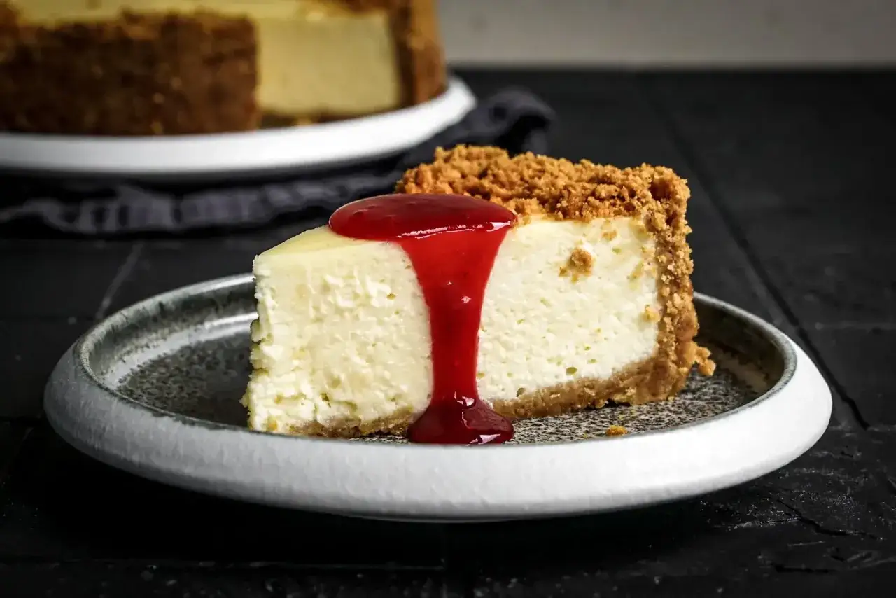 Ein St&uuml;ck cremiger American Cheesecake mit Keksboden und roter Fruchtsauce. Das perfekte Rezept f&uuml;r originalen American Cheesecake.