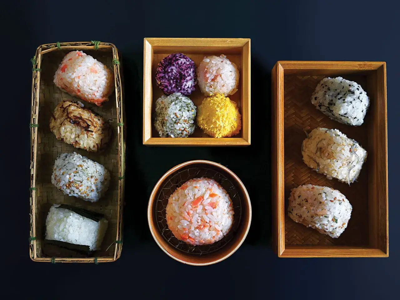 Vielfalt an japanischen Gerichten mit Reis: bunte Onigiri in Körbchen und Schalen, mit Lachs, Algen und Sesam.