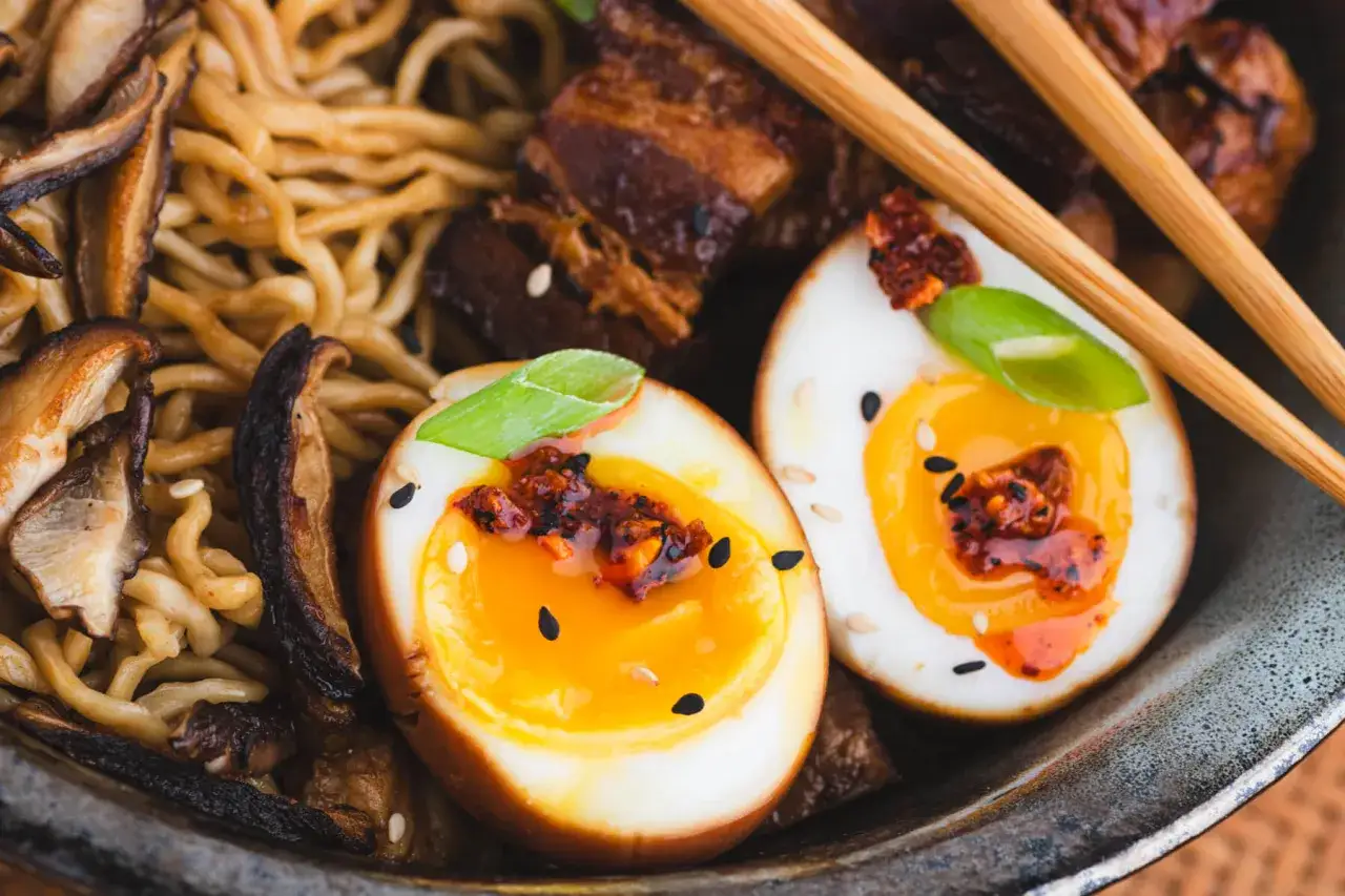 Ramen-Schüssel mit Nudeln, Pilzen, Fleisch und perfekt gekochten, halbierten ramen eiern, garniert mit Frühlingszwiebeln und Sesam.