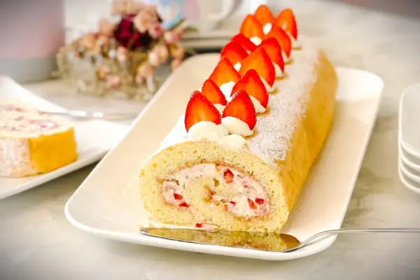 Ein köstlicher Brazo de Reina, gefüllt mit Sahne und Erdbeeren, dekoriert mit frischen Erdbeeren und Puderzucker.