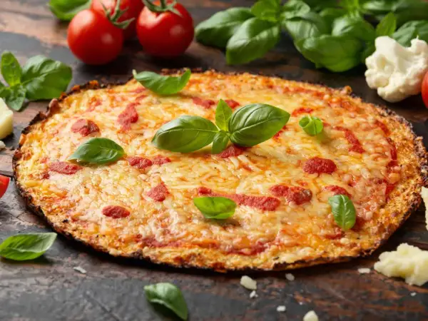 Eine köstliche blumenkohl pizza vegan, belegt mit Tomaten und Käse, garniert mit frischem Basilikum.