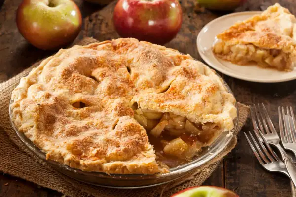 Goldbrauner Apfelkuchen, ein Klassiker der american pie recipe, mit saftiger Füllung und knusprigem Teig. Daneben Äpfel und Gabeln.