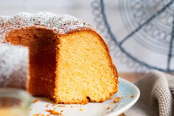 Saftiger Kuchen mit 12 Eiern, bestäubt mit Puderzucker, auf einem Teller mit einem Stück herausgeschnitten.