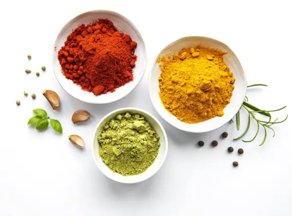 Schalen mit roten, gelben und grünen Gewürzen, Knoblauch und Kräutern – die Zutaten, woher kommt Curry.