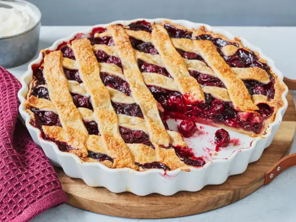 Ein frisch gebackener Kirschkuchen mit Gittermuster, perfekt für ein Kirschkuchen Rezept. Daneben eine Schüssel Schlagsahne.