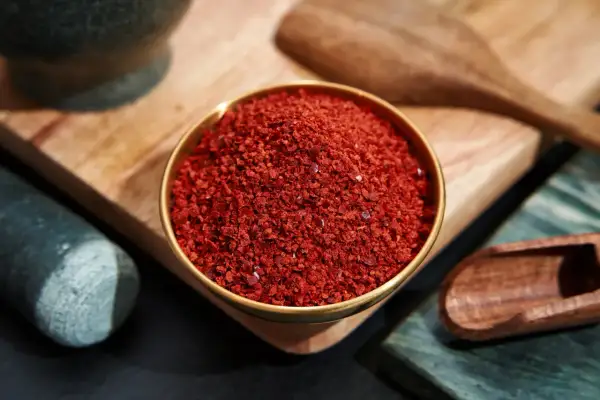 Schüssel mit leuchtend rotem Cayennepfeffer, bereit zum Würzen. Daneben ein Mörser und ein Holzschaber.