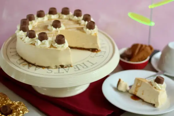 Eine köstliche karamell torte, verziert mit Sahnetuffs und Schokoladenstückchen, steht auf einem Tortenständer. Ein Stück ist bereits auf einem Teller angerichtet.
