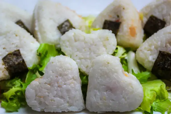 Herzförmige und dreieckige japanische Gerichte mit Reis, umhüllt von Nori-Algen, serviert auf knackigem Salat.