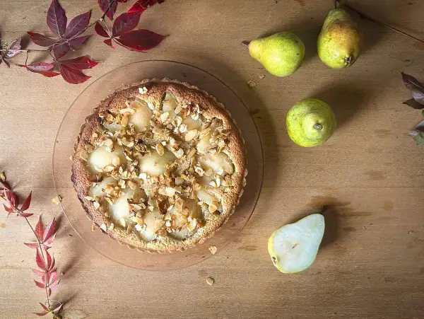 Eine köstliche Tarte Bourdaloue mit Birnen und Mandelsplittern, umgeben von frischen Birnen und herbstlichen Blättern auf Holzhintergrund.