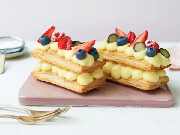 Zwei Mille-feuille-Törtchen mit Vanillecreme und frischen Beeren, bereit zum Genießen.