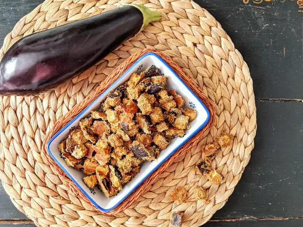 Knusprige, frittierte Aubergine in einer Schale, daneben eine ganze Aubergine. Ein leckerer Snack!