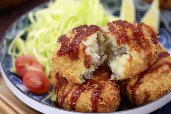 Knusprige japanische Kroketten, gefüllt mit Kartoffelpüree und Hackfleisch, serviert mit Salat und Tomaten.