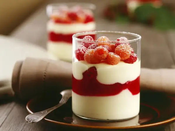 Zwei Gläser mit Schichten von Mousse au Chocolat Blanc, Himbeersauce und frischen Himbeeren, bestäubt mit Puderzucker.