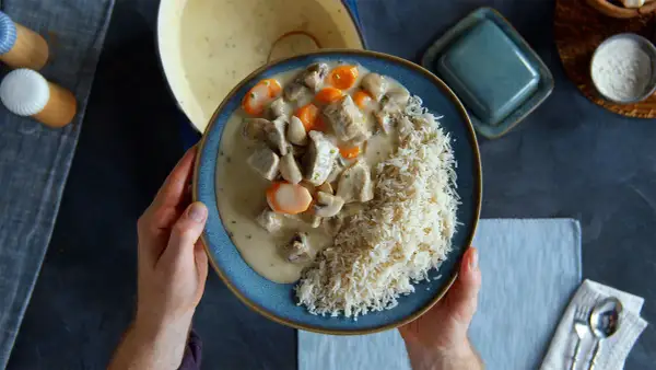 Ein Teller mit cremigem Blanquette de veau, Pilzen und Karotten, serviert mit Reis.