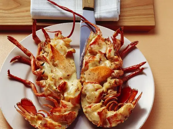 Zwei Hälften Hummer Thermidor, überbacken mit cremiger Sauce und Gewürzen, auf einem Teller angerichtet.