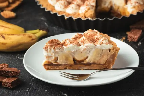 Ein Stück Banoffee Pie mit Bananen, Karamell und Sahne, bestreut mit Kakaopulver. Perfekt für Ihr Banoffee Pie Rezept!