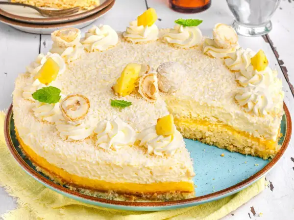 Ein köstlicher Ananas Kokos Kuchen, verziert mit Kokosraspeln, Sahnetuffs, Ananasstücken und Minze.