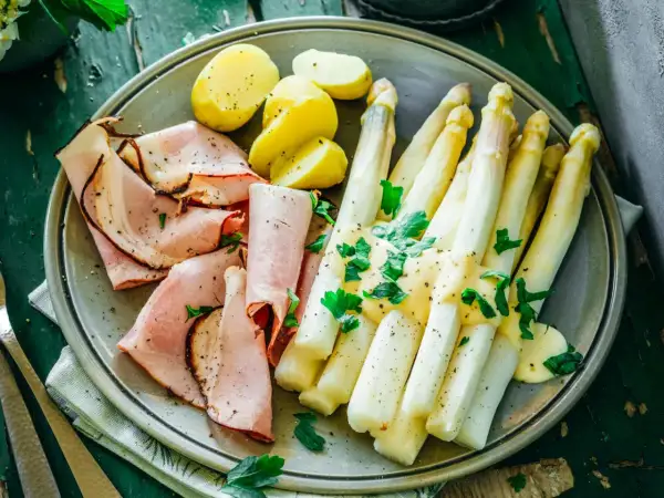 Ein Teller mit gekochtem Spargel, Schinken und Kartoffeln, garniert mit Petersilie. Perfekt für die besten Spargelrezepte!