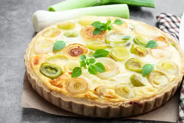 Herzhafte Quiche aux poireaux mit goldbraunem Teig und frischen Lauchringen, garniert mit grünen Kräutern.