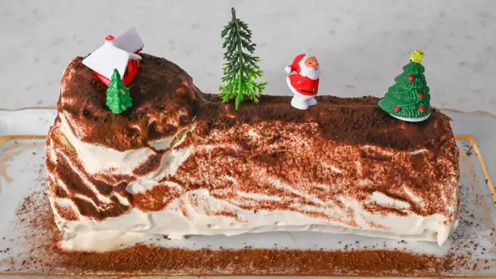 Eine festliche Bûche de Noël, dekoriert mit Weihnachtsmann, Bäumen und einem Haus.