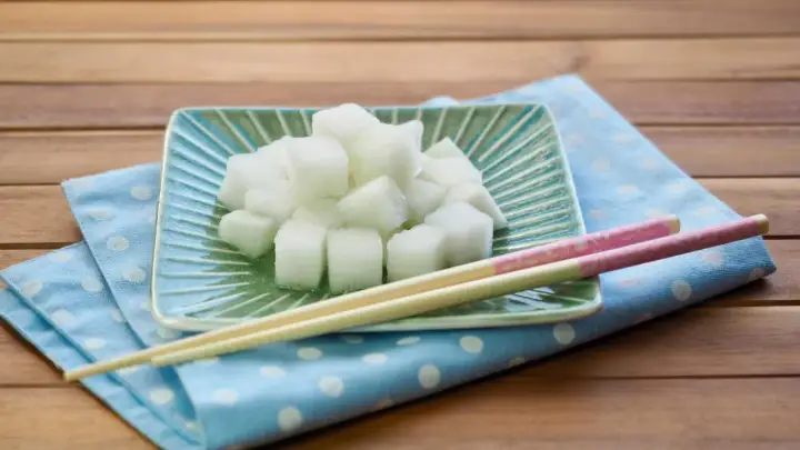 Würfel von daikon rettich auf einem grünen Teller, daneben Stäbchen auf einem blauen Tupftuch.
